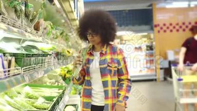 非洲女人留着非洲发型，手里拿着手机，在超市里挑选蔬菜